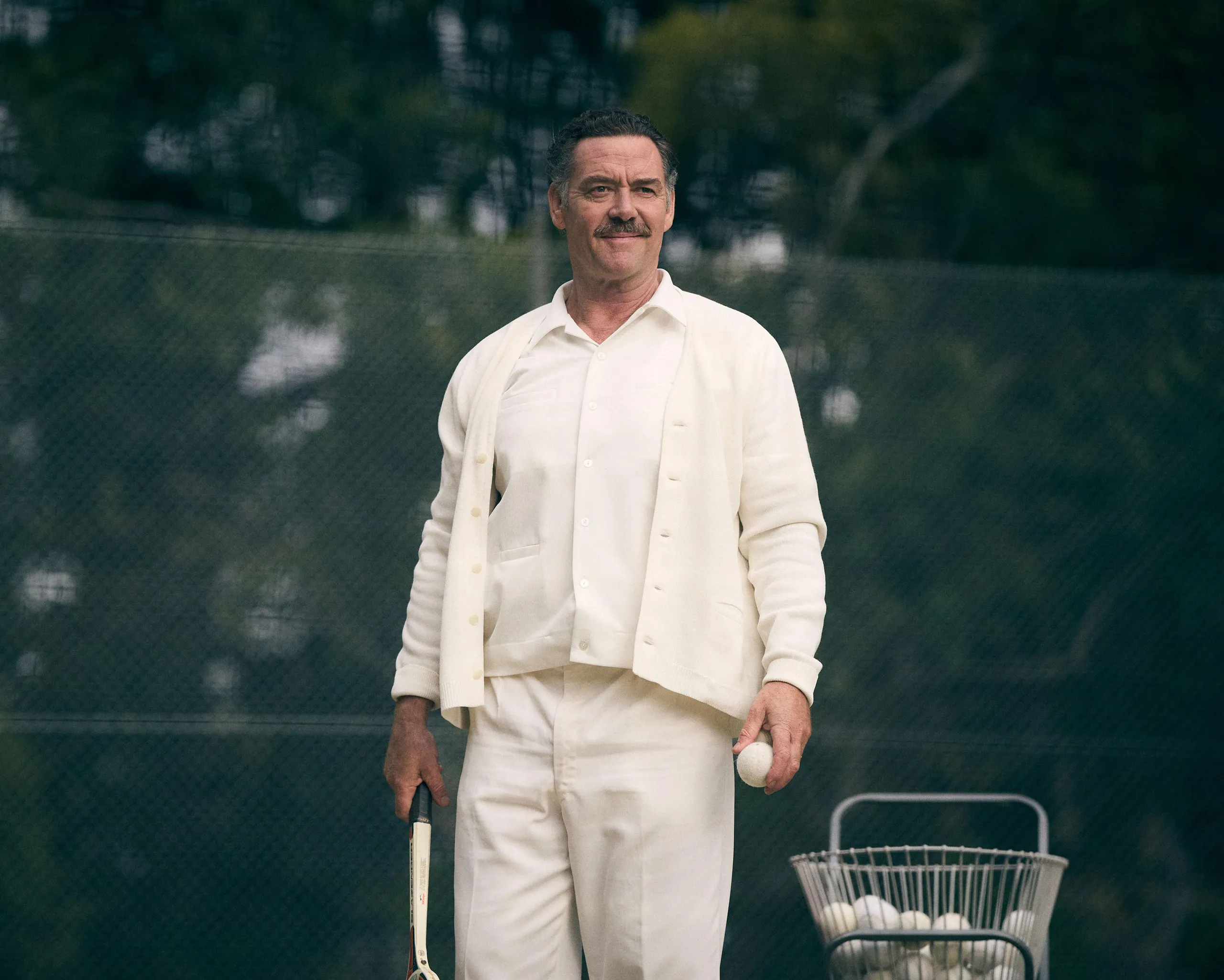 a man standing next to a basket of tennis balls wearing all white