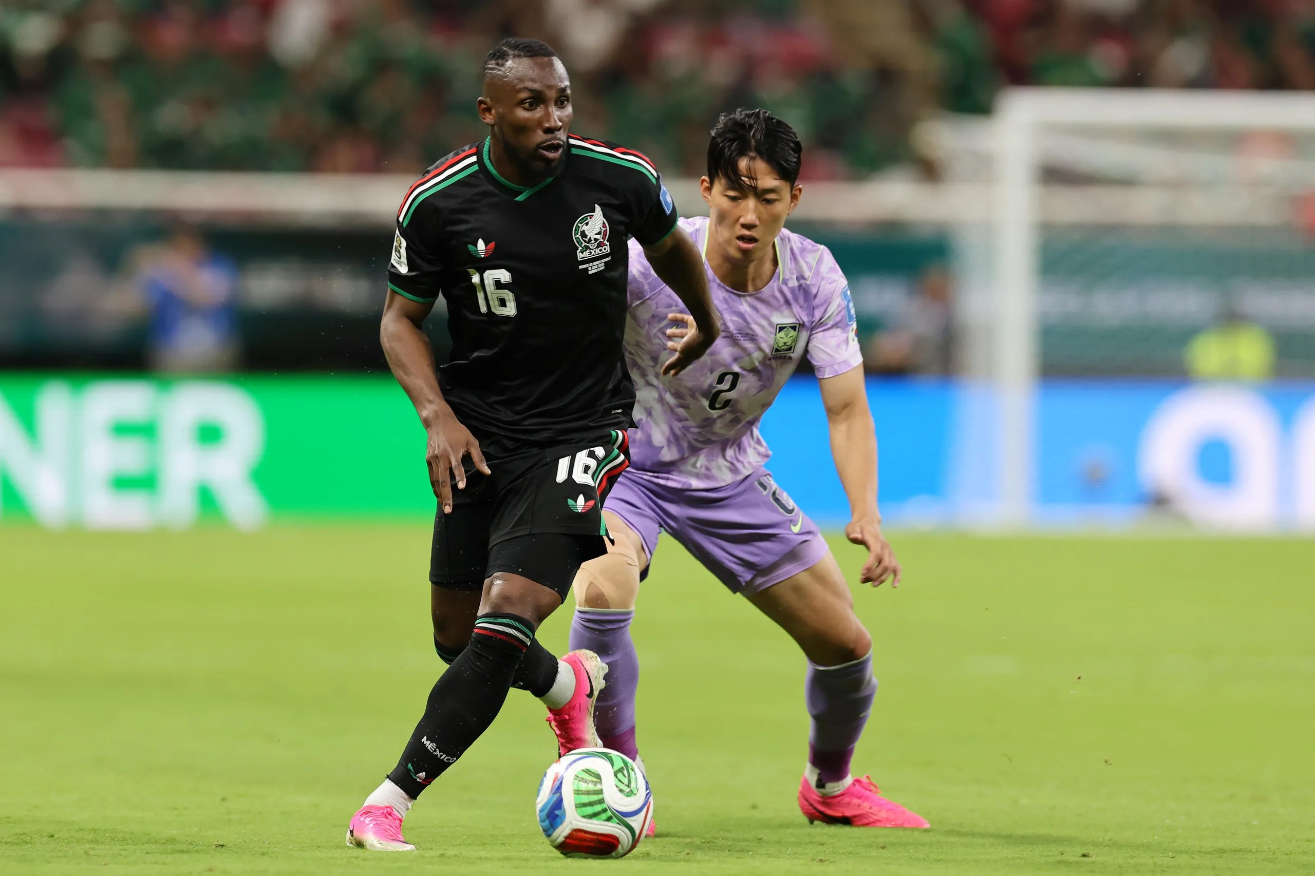 Julián Quiñones, wearing a black jersey and shorts, dribbles against a South Korea defender in their World Cup match.