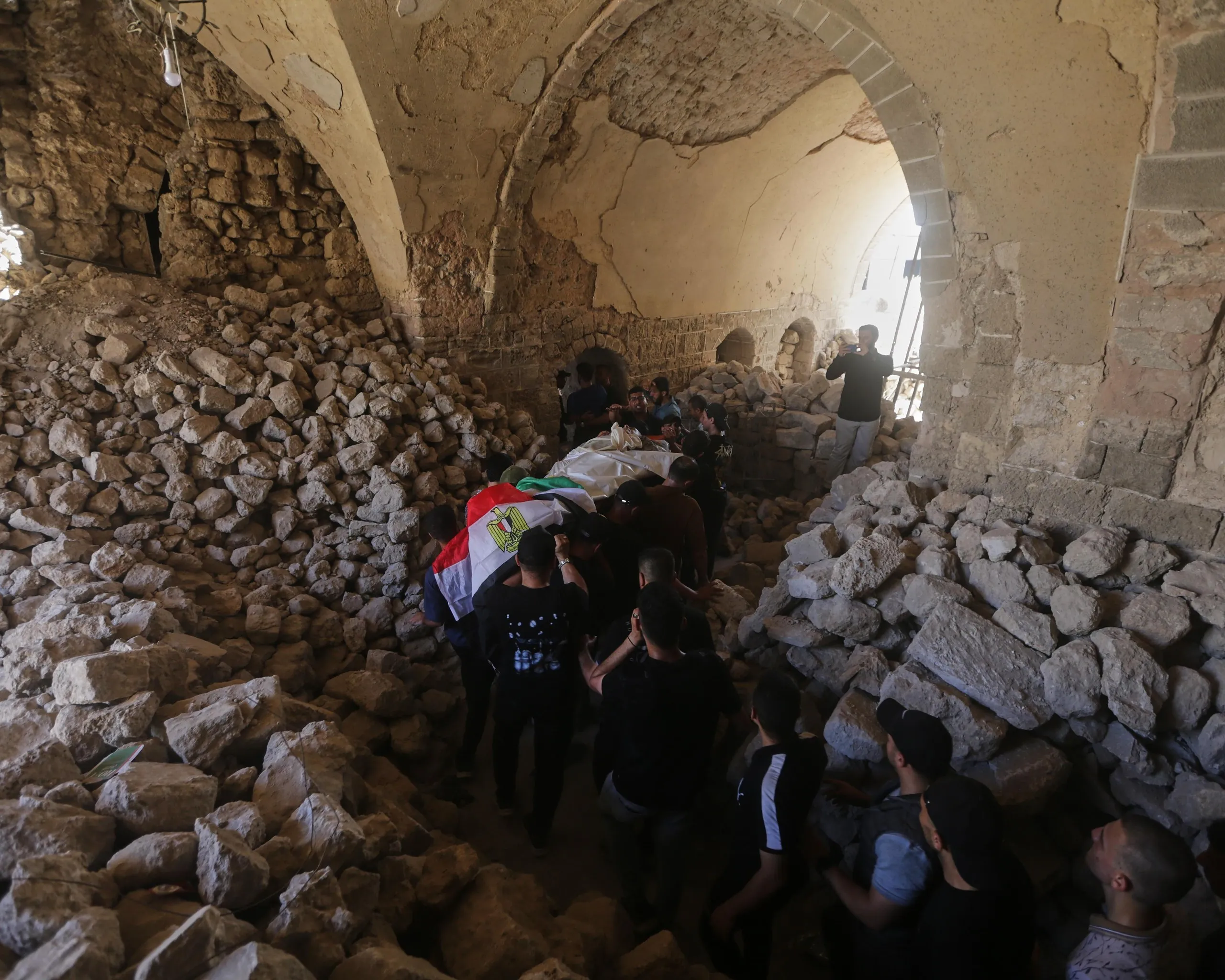 A funeral procession bearing a body wrapped in the Egyptian flag makes it way through a mosque filled with rubble